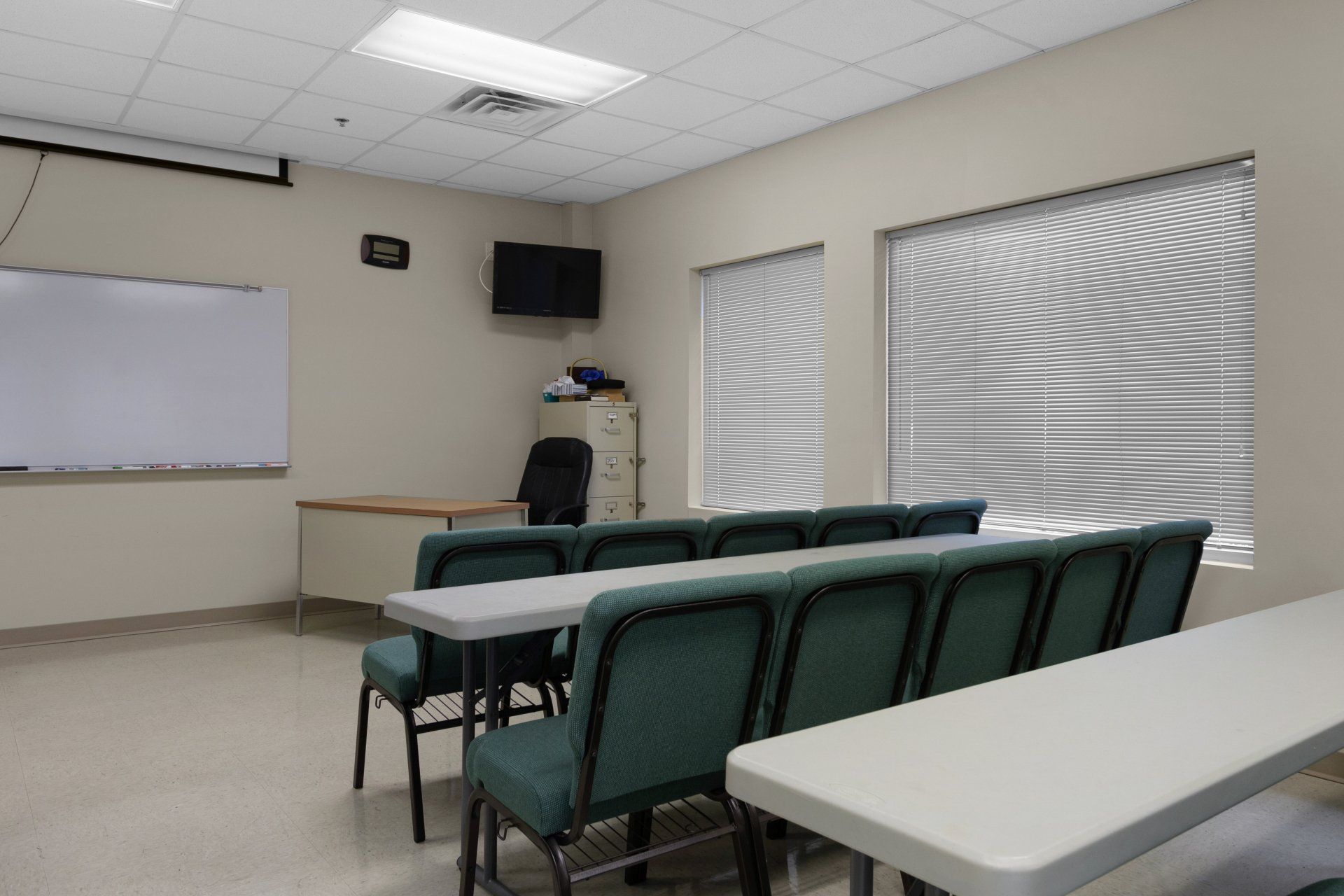 Empty classroom with rows of chairs and tables, a whiteboard, and a TV.