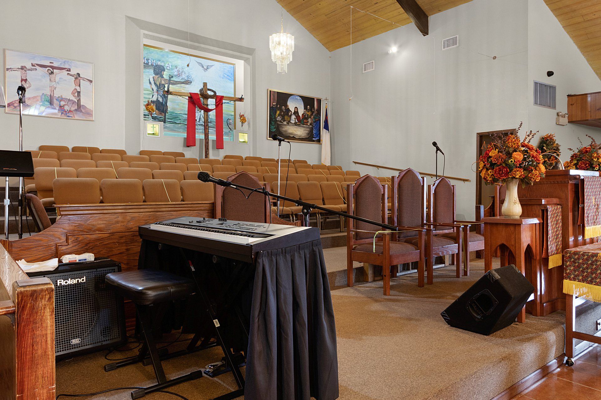 Interior of a church sanctuary, with rows of pews, a stage with a keyboard, and religious artwork.