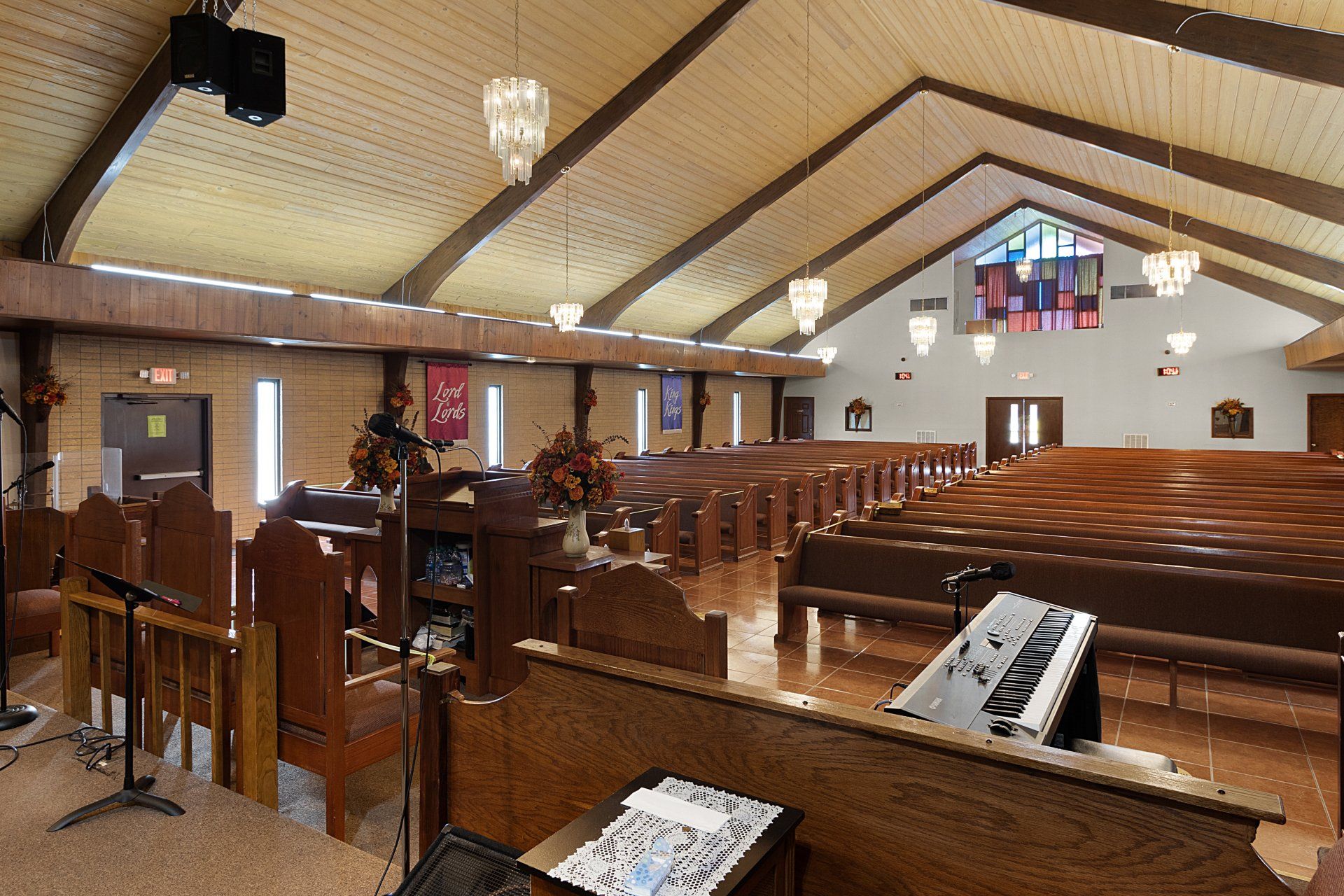 Interior of a church with wooden pews, high angled ceiling, and stained-glass window.
