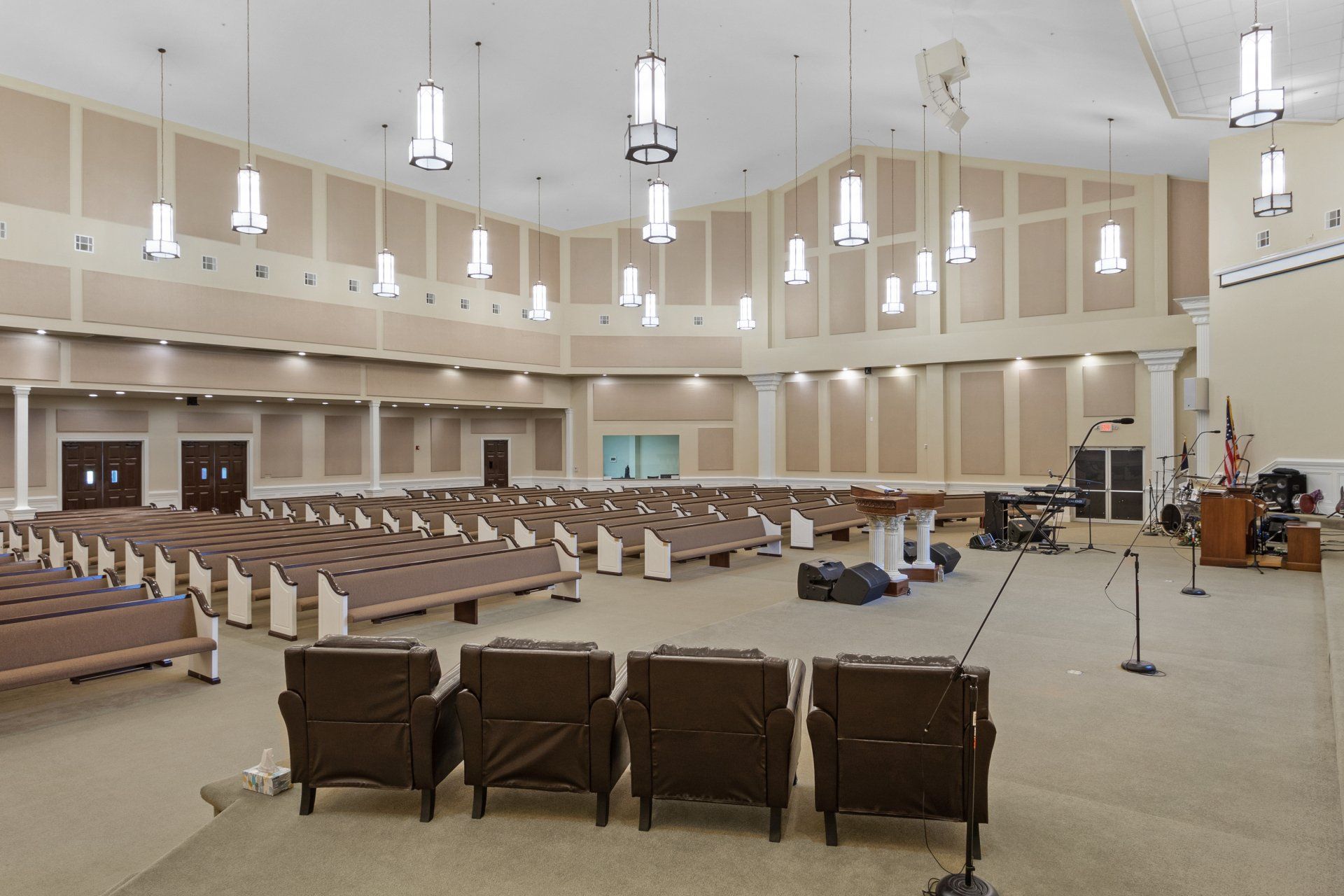 Empty church auditorium with rows of pews, stage with chairs, and hanging lights.