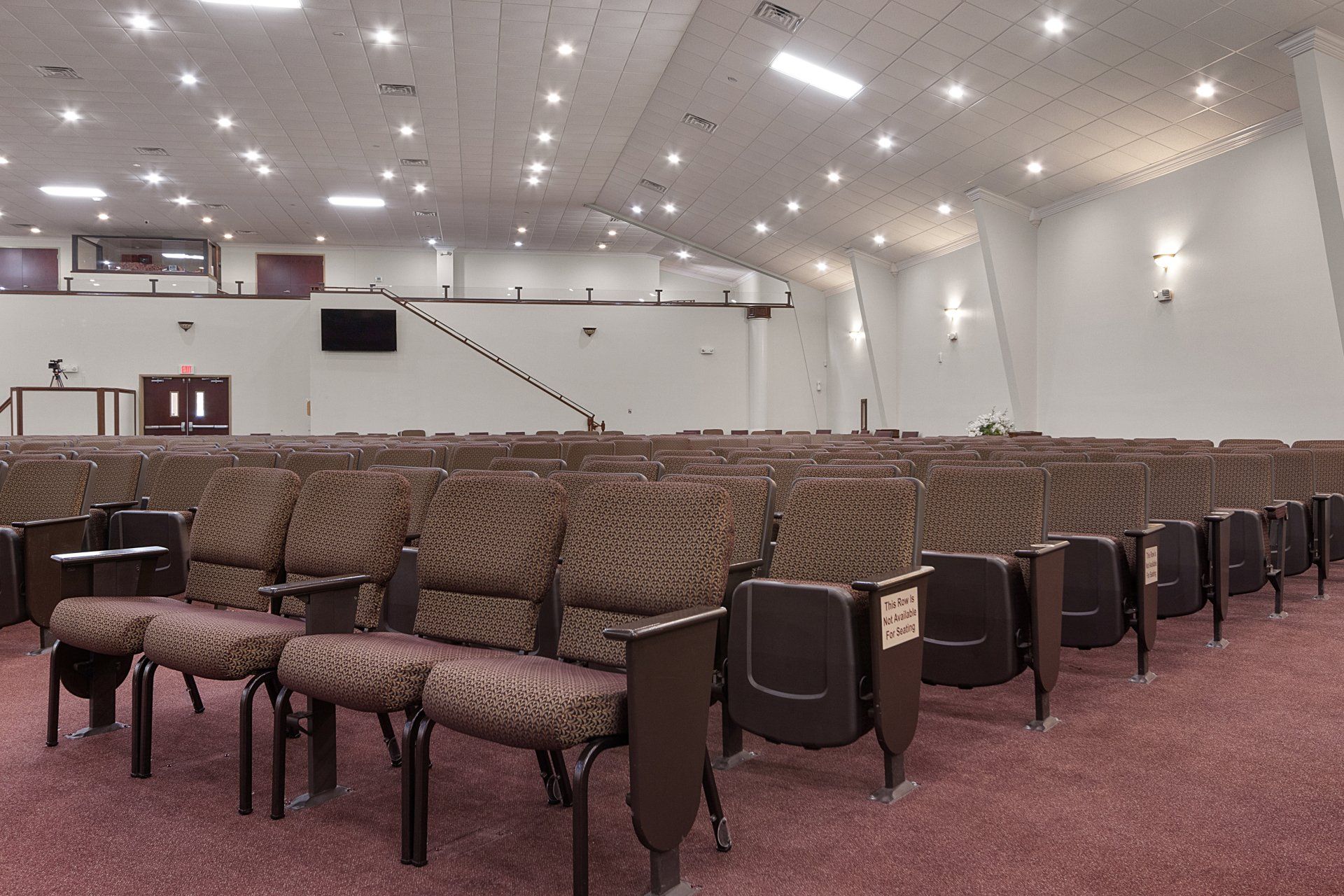 Auditorium with rows of brown patterned seats, a stage area, and overhead lights.