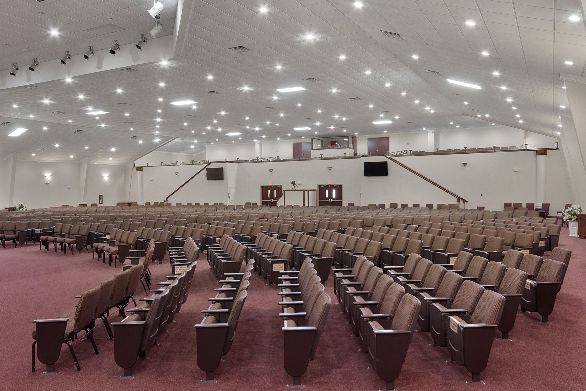 Large, empty auditorium with rows of brown seats, stage at the front, many overhead lights.