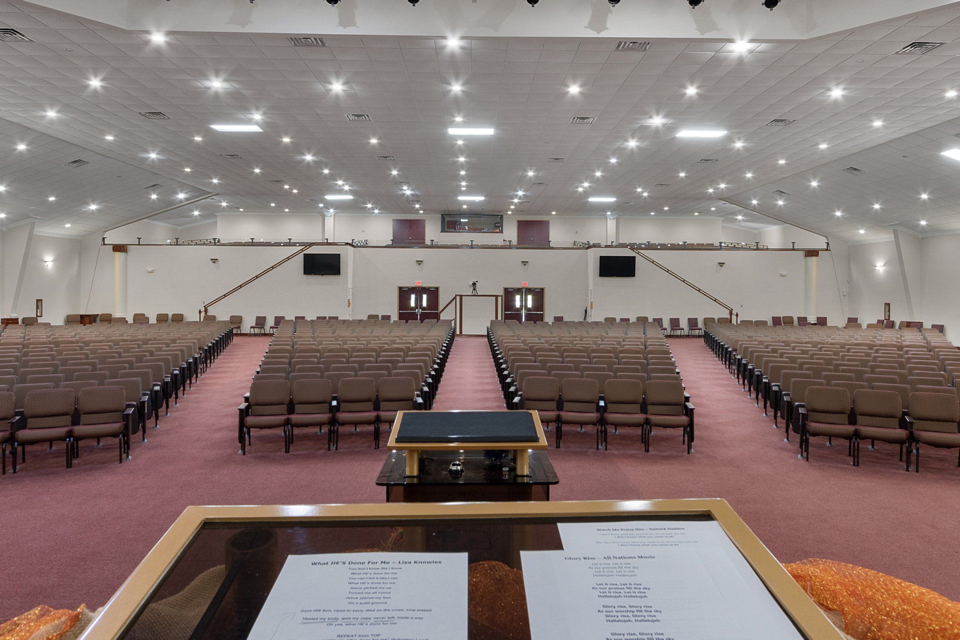 Empty church interior with rows of seats, pulpit, and high ceiling lights.