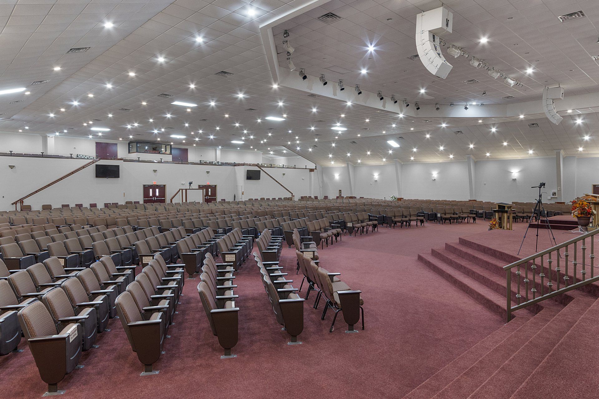 Large, empty auditorium with rows of brown seats, red carpet, and bright lights on the ceiling.