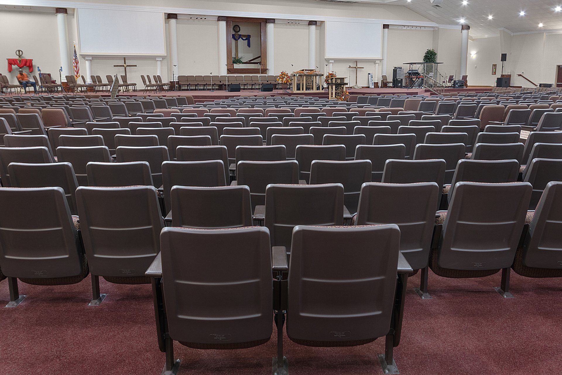 Rows of brown chairs fill a large auditorium. A stage is at the far end.