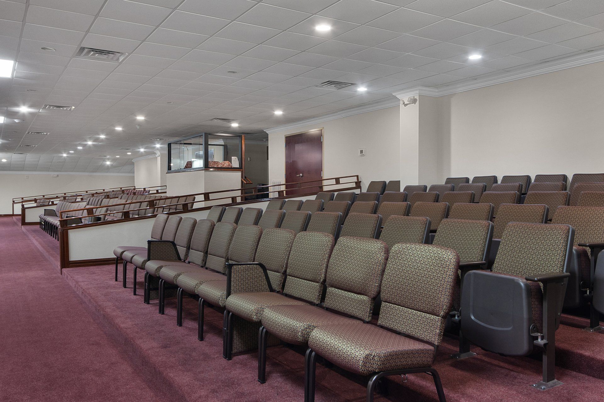 Rows of empty seats in a large room with a red carpet and overhead lighting.