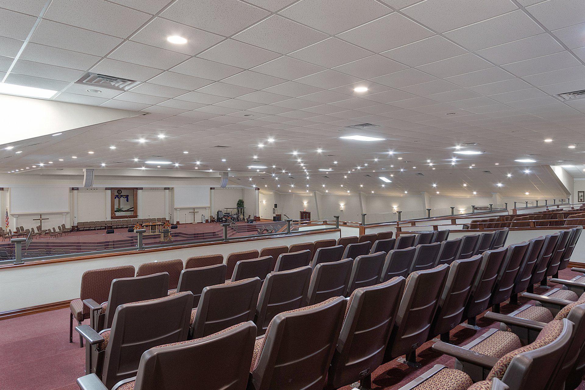 Auditorium with rows of brown seats, stage at the far end, and a white ceiling.