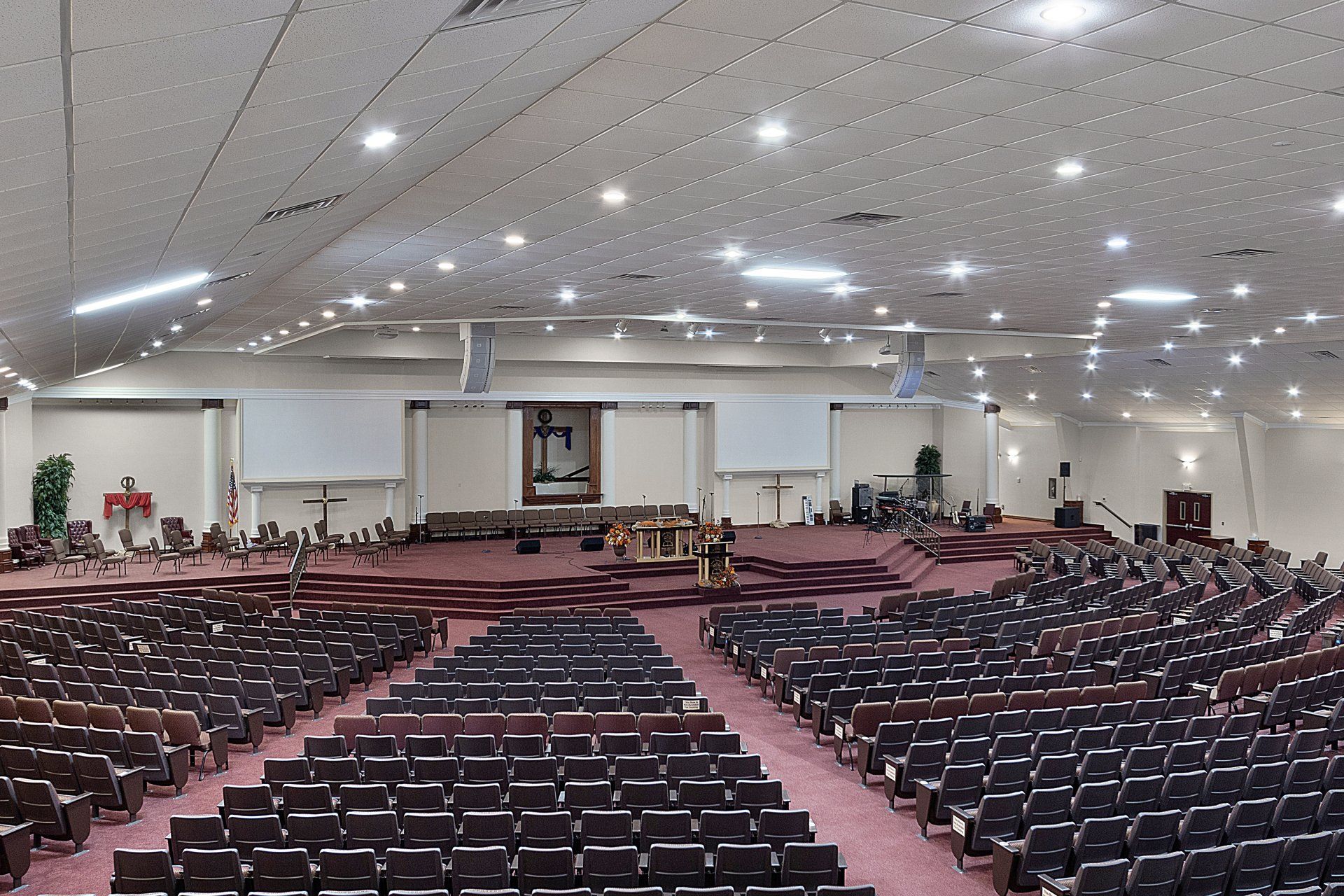 Large auditorium with rows of seating facing a stage; stage has a cross and instruments.