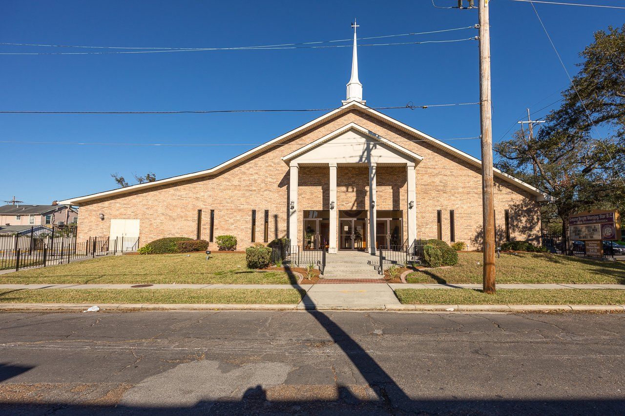 Church building with beige brick facade, white steeple, and green lawn.