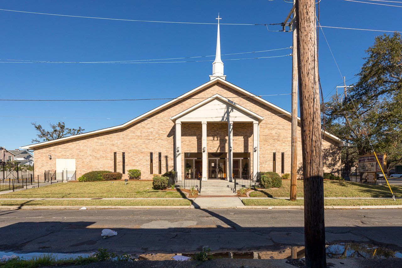 Brick church with steeple and columns under a clear blue sky.