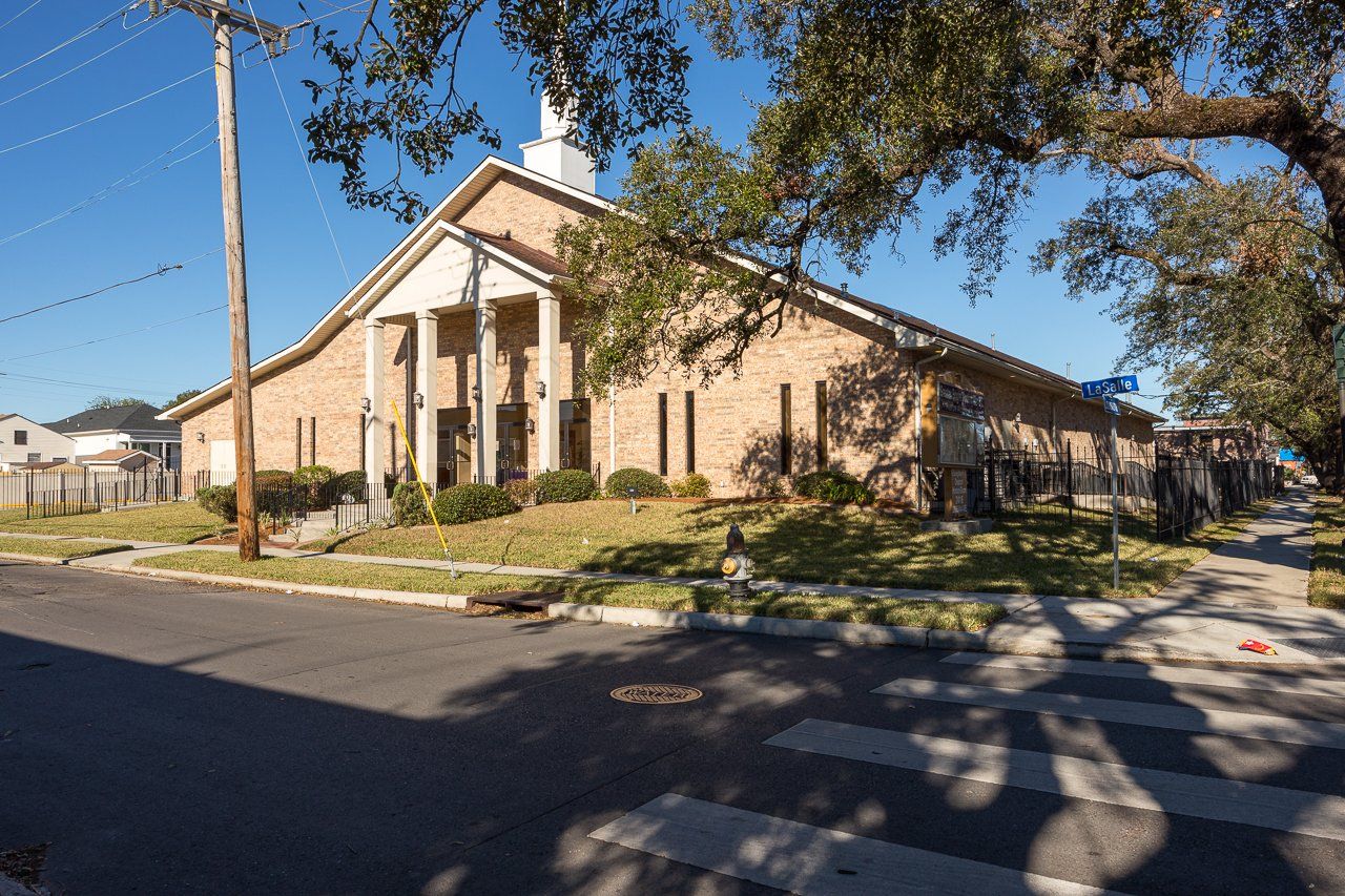Brick church building with white columns and steeple; sunny day.