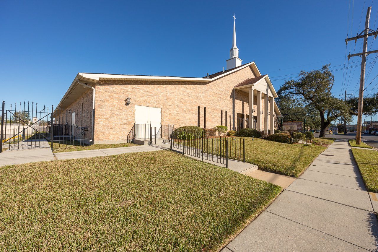 Brick church with steeple, grassy yard, and sidewalk under a blue sky.