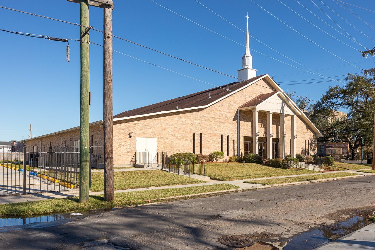 Brick church building with white steeple, columns, and a brown roof under a clear blue sky.