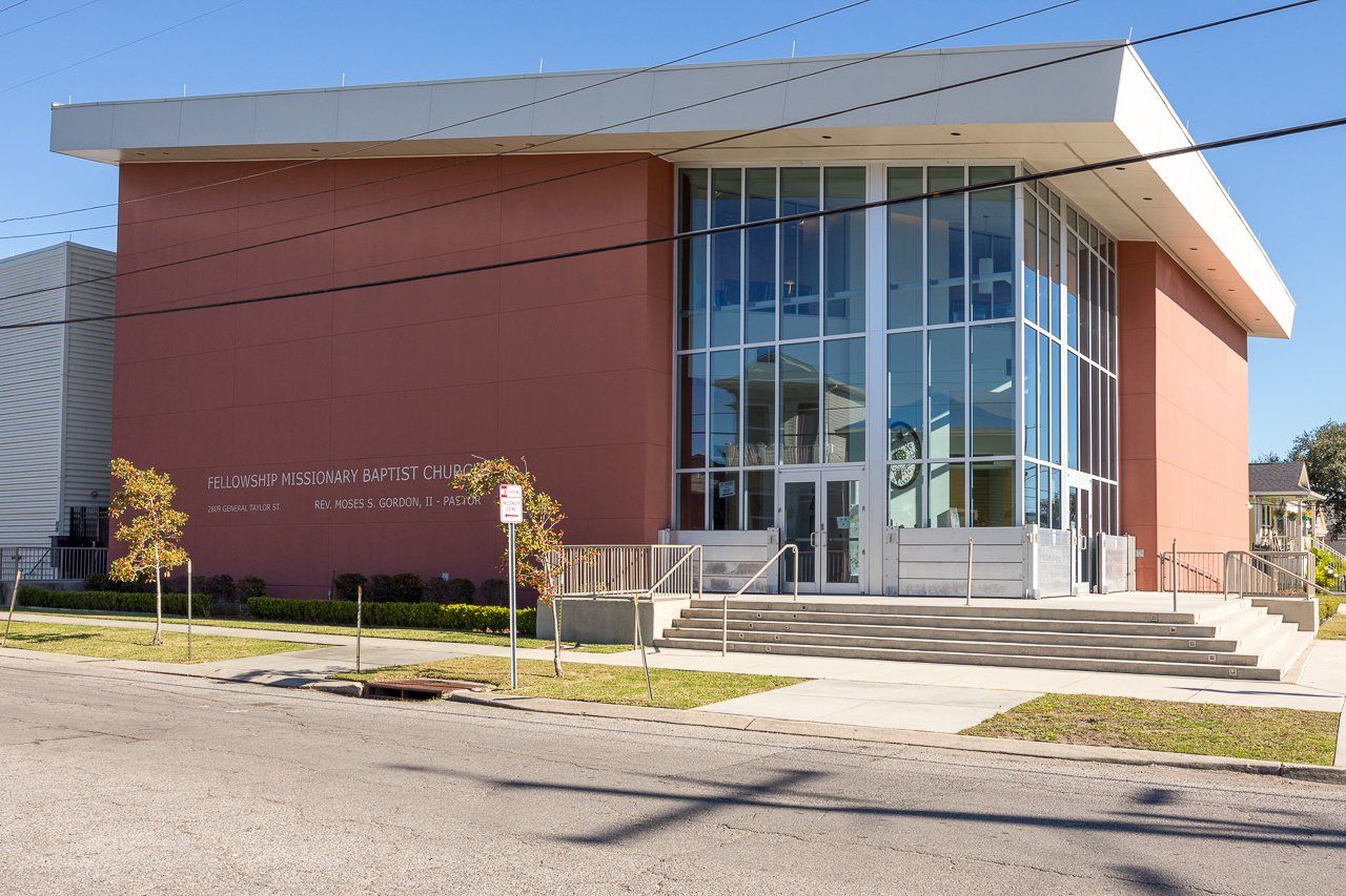 Building with red brick walls, large glass windows, and a white flat roof. Steps lead to the entrance.