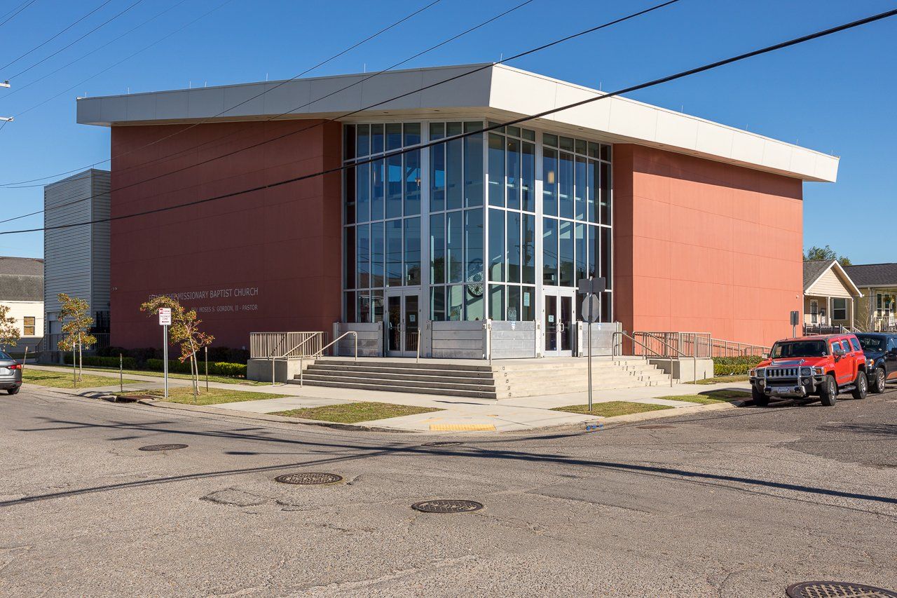 Building with glass front entrance, brick walls, and white overhang on a street corner under a sunny sky.