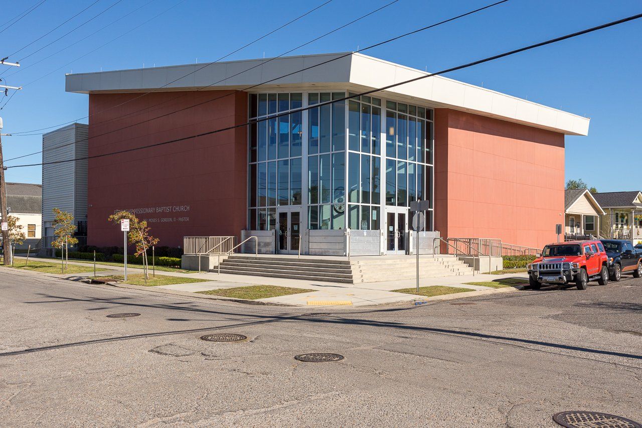 Brick building with large glass entrance, concrete walkway, red car parked outside.