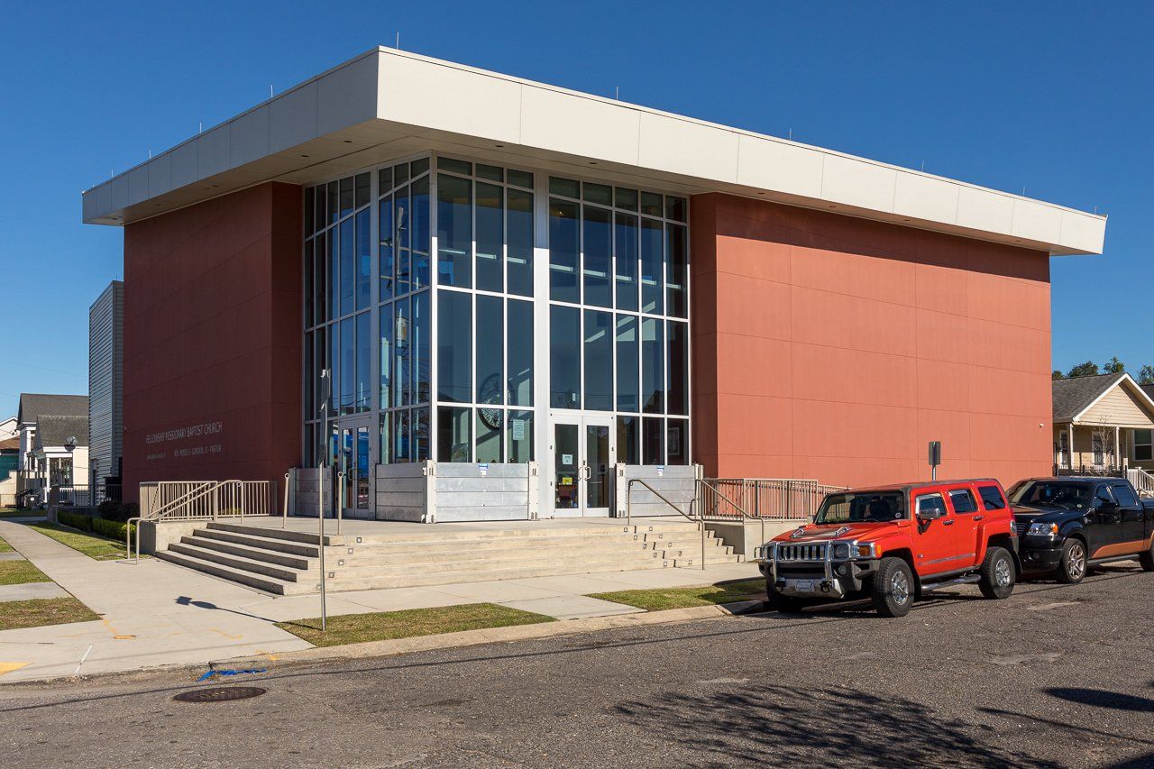 Modern brick building with large glass entrance, red SUV parked in front.