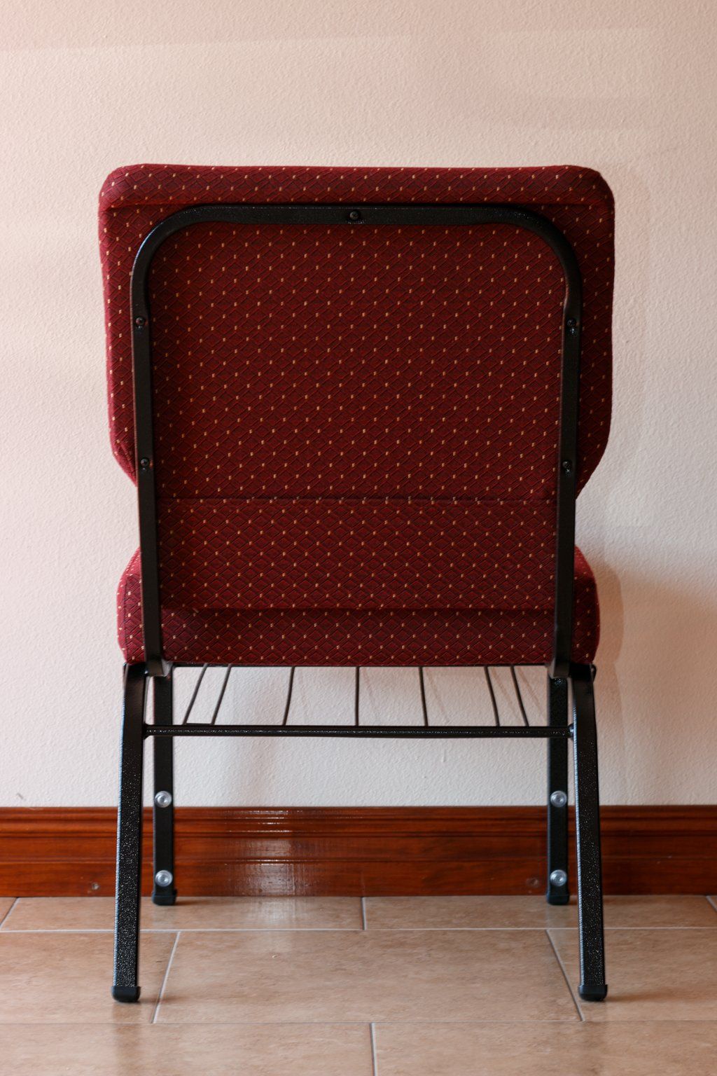 Back view of a red patterned chair with a black metal frame, placed against a cream wall and wood trim.