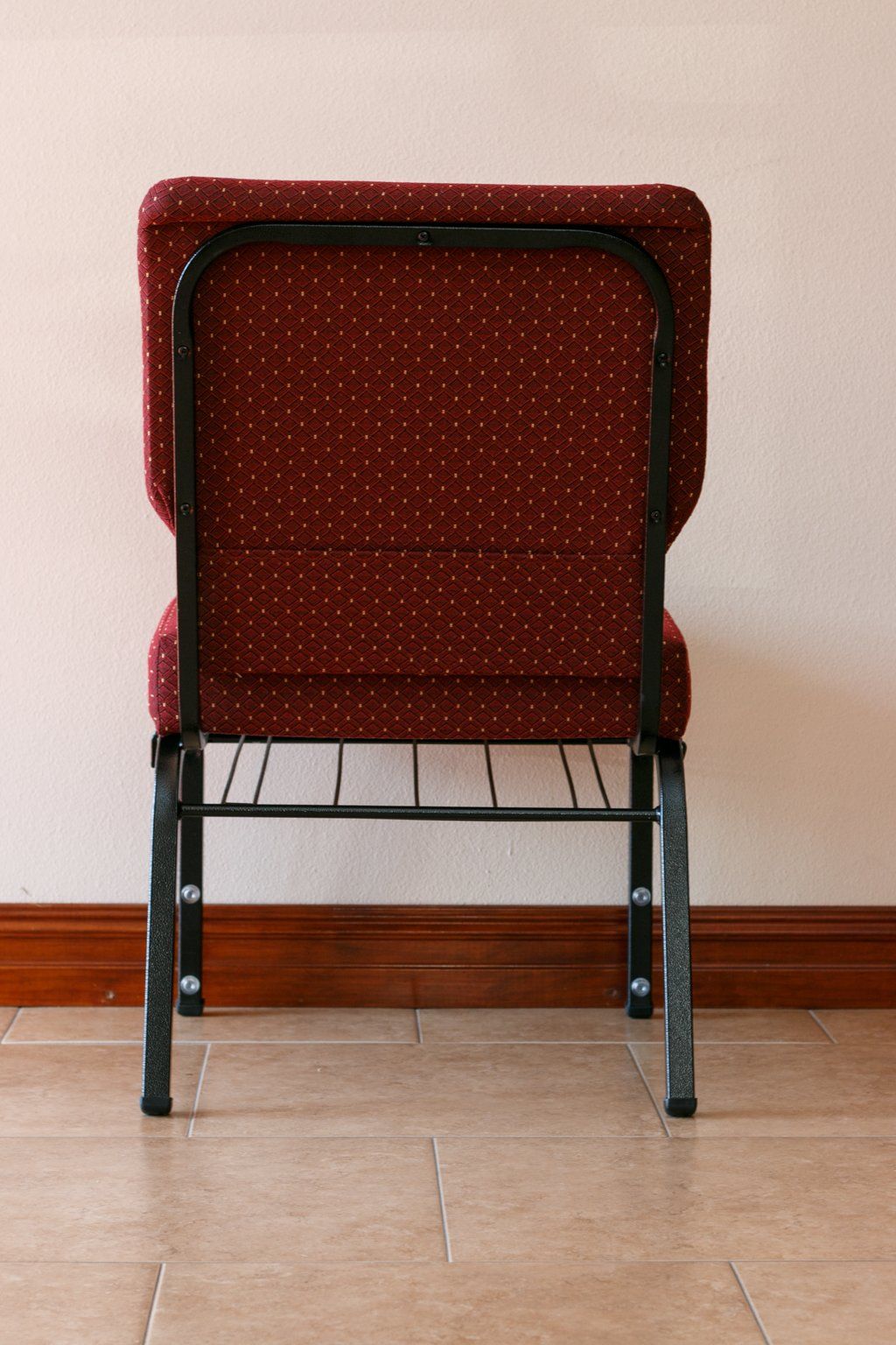 Back of a burgundy fabric chair with a black metal frame, against a cream wall.