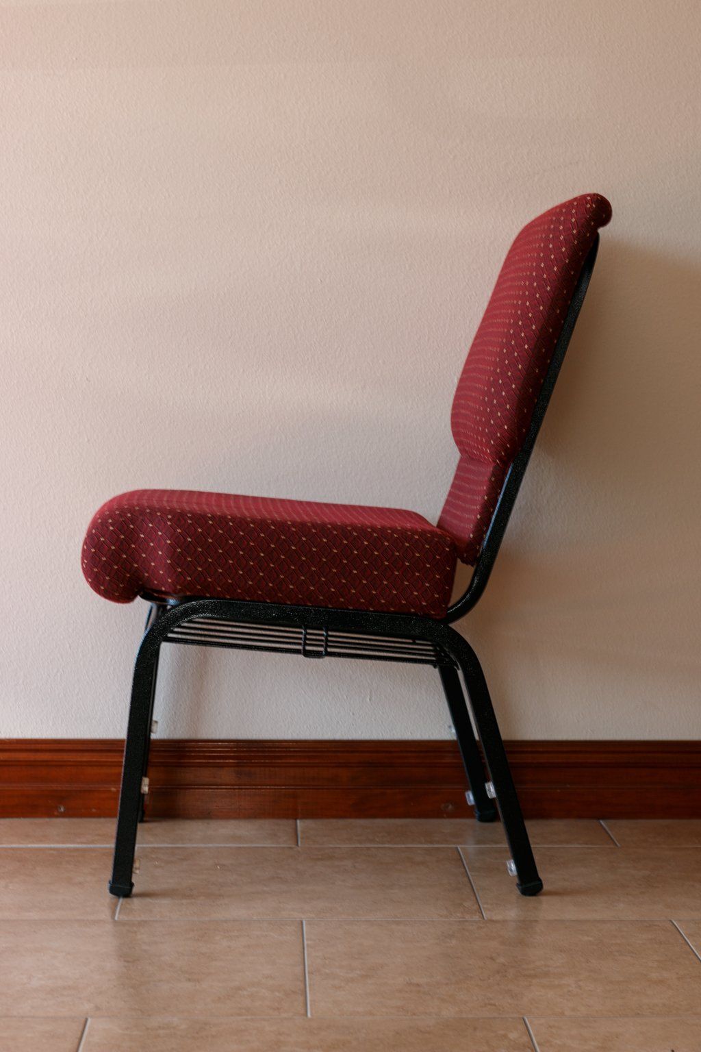 Red upholstered chair with black metal frame, set against a cream wall and wooden baseboard.