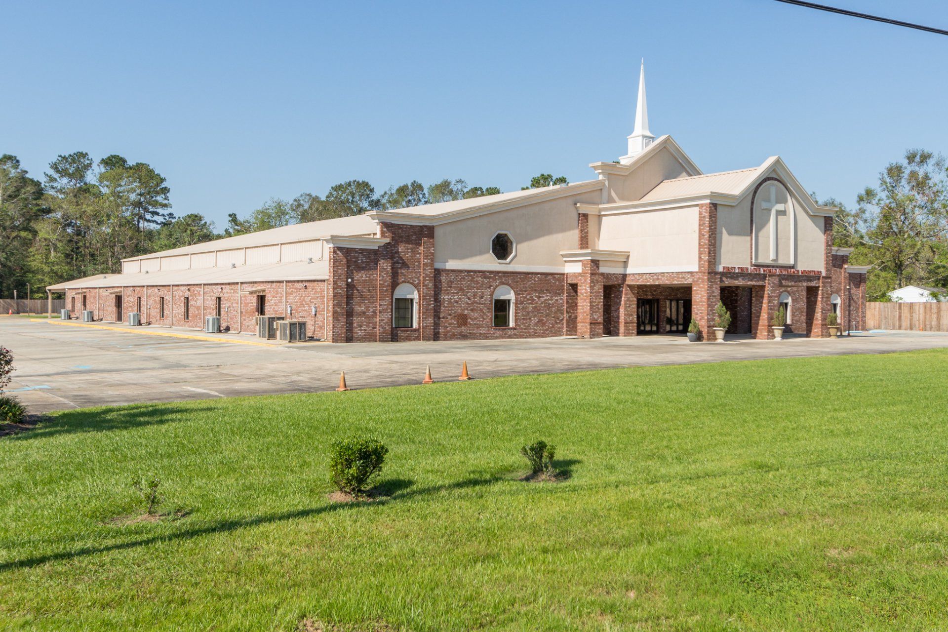 Brick and beige church building with a steeple, set on a green lawn, and clear blue sky.