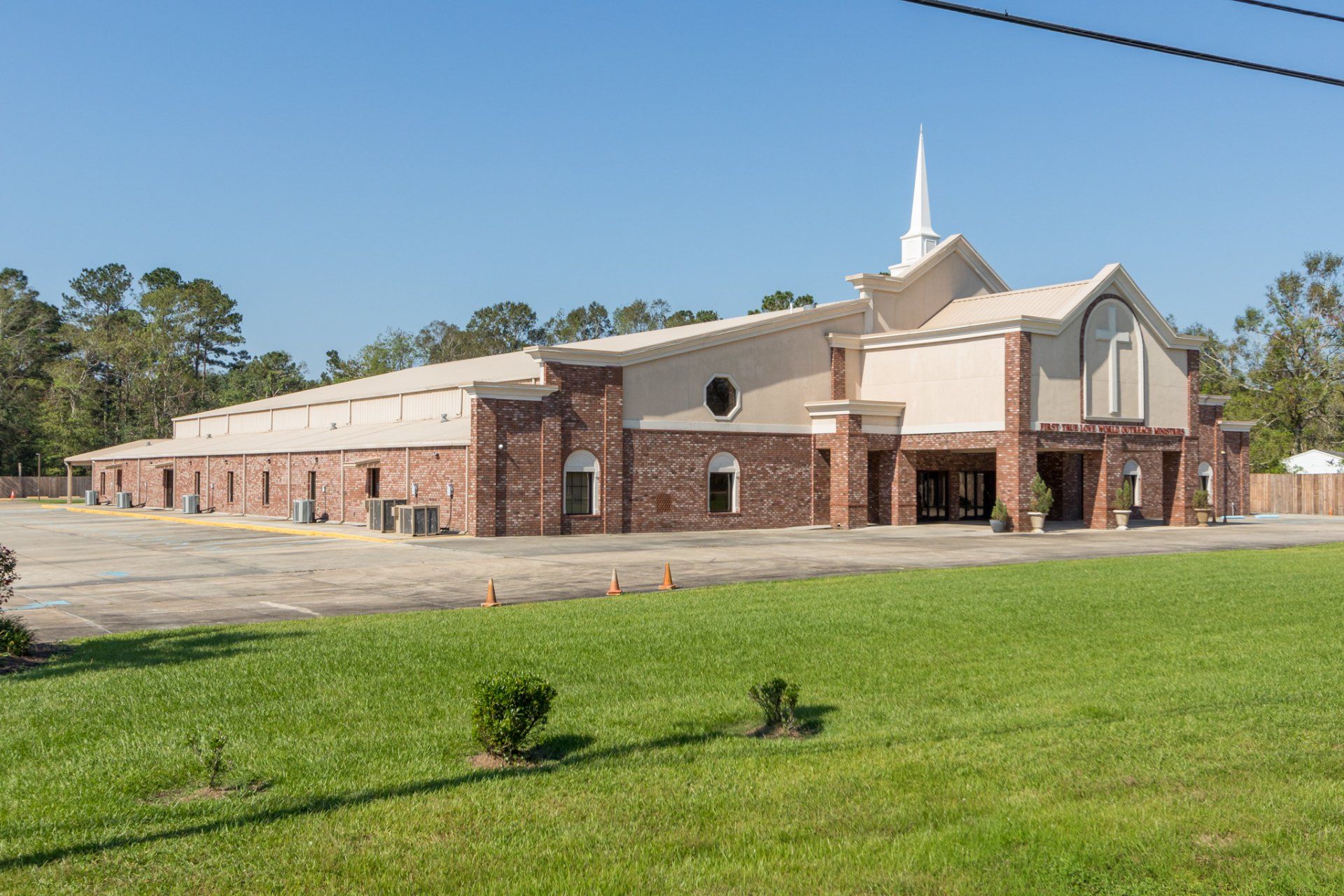 Church building with red brick and beige facade, white steeple, on green grass, clear sky.