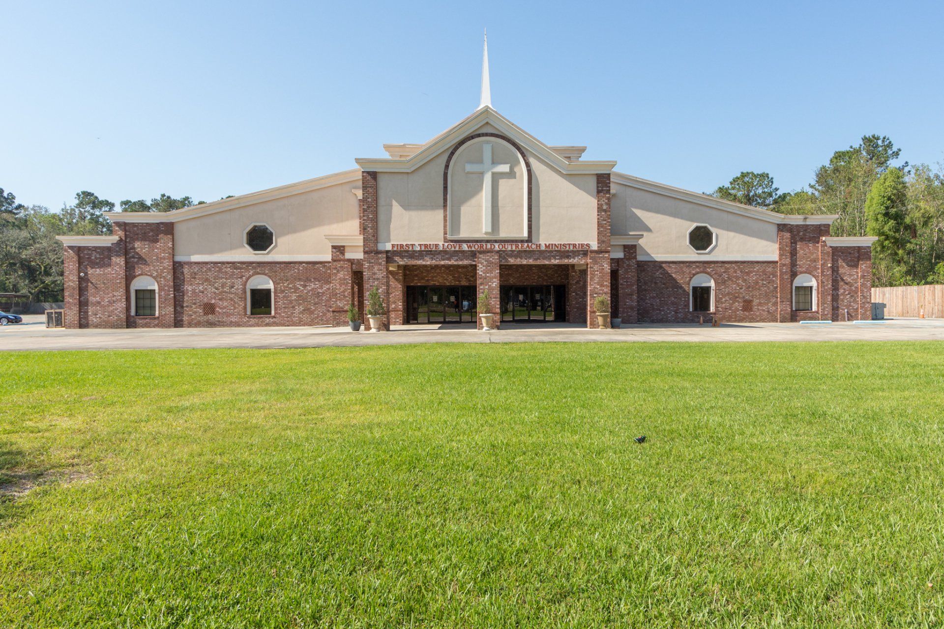 Church building with a white cross on the front facade and a large lawn in front.