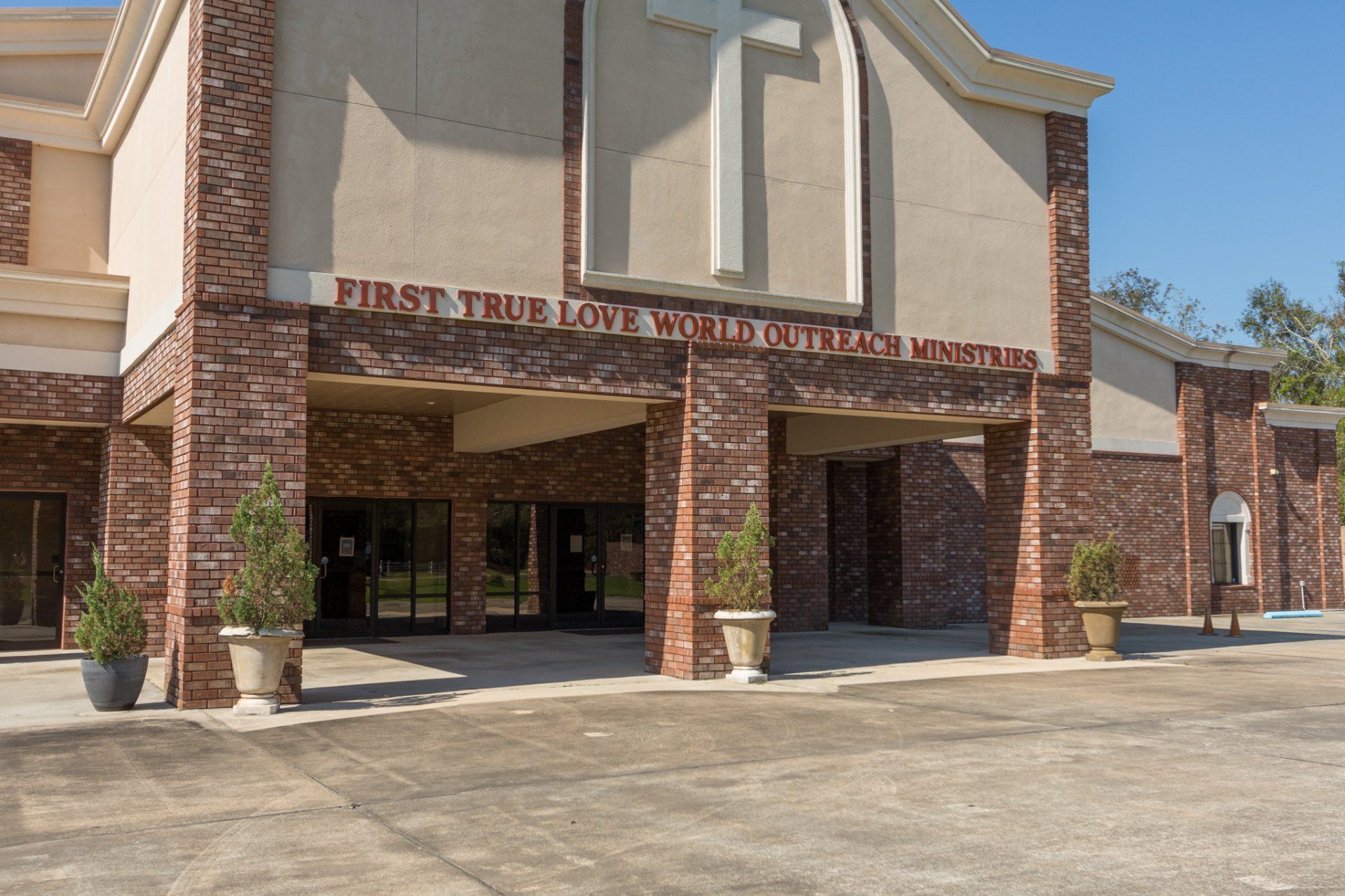 Church exterior with red brick, beige facade, and a cross. 