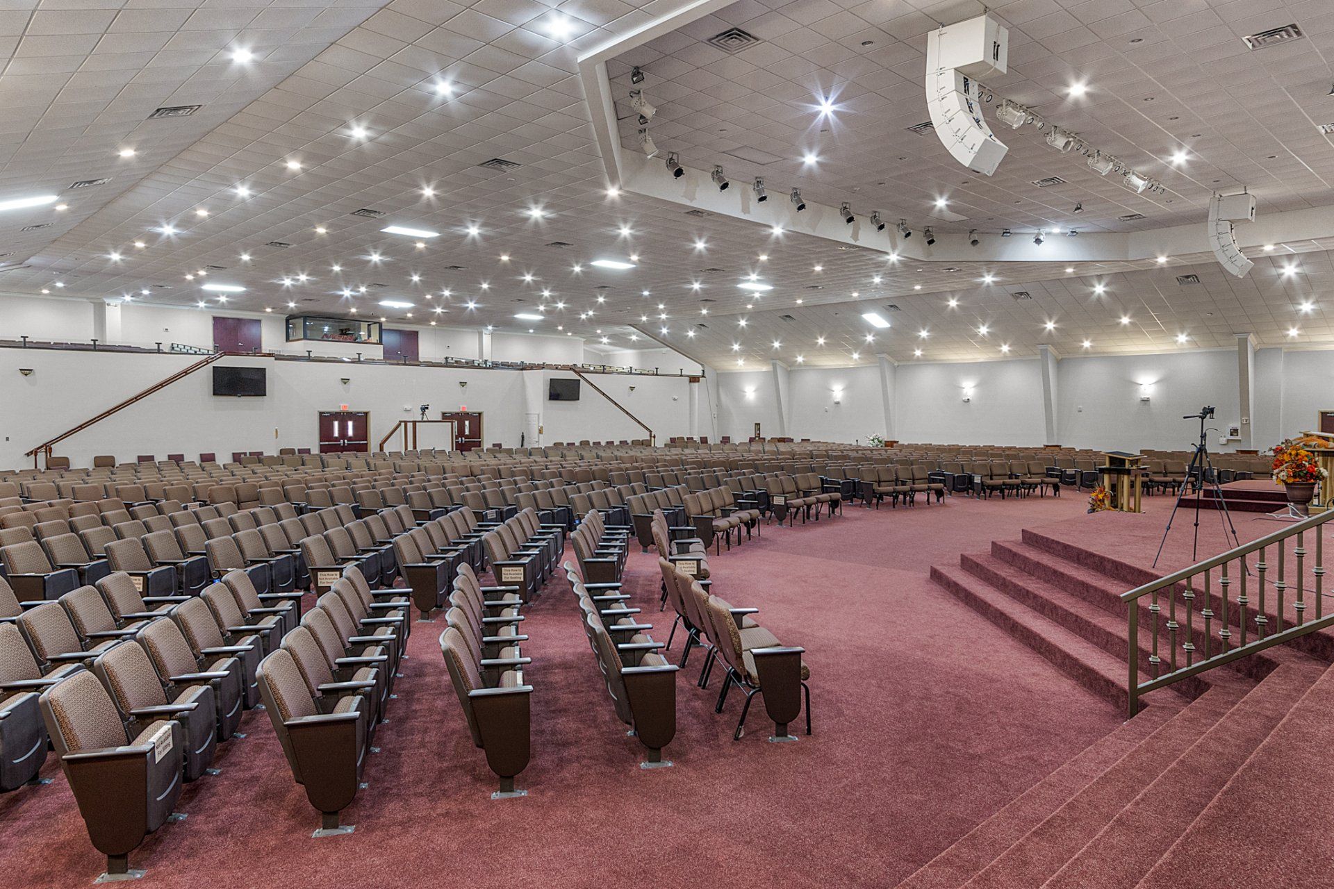Large auditorium with rows of seats, red carpet, and stage, under bright lights.