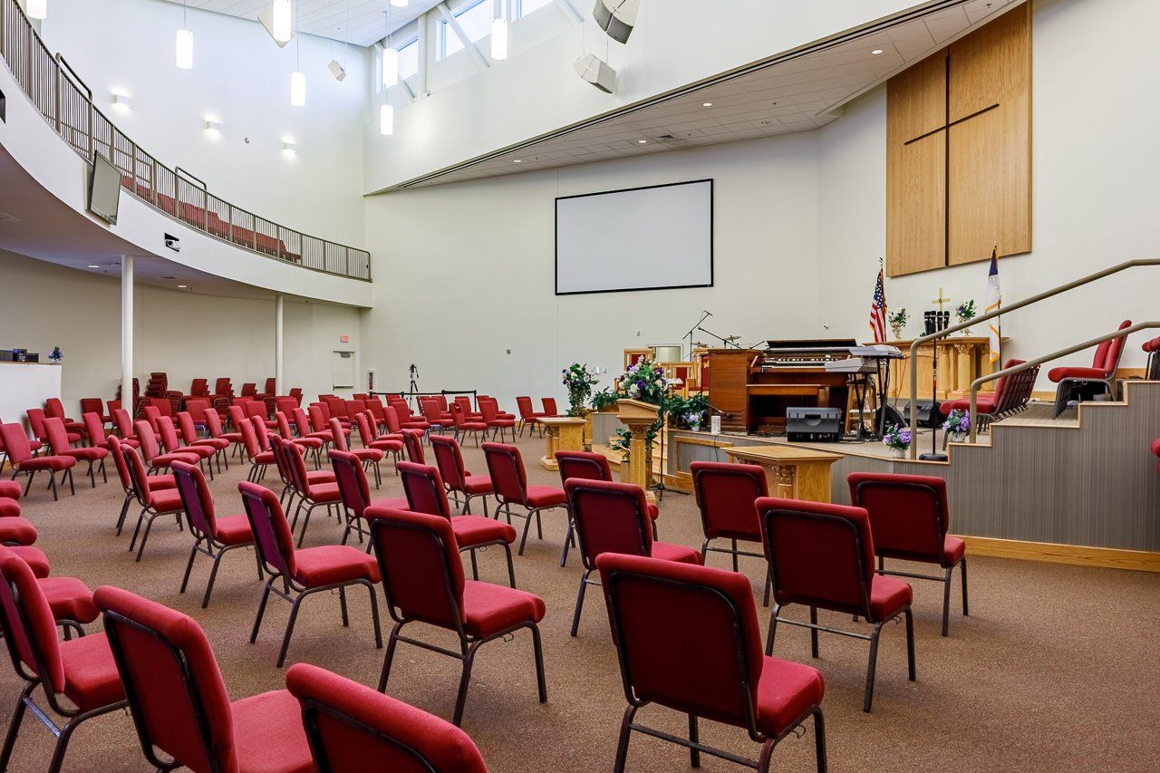 Empty church auditorium with red chairs facing a stage, screen, and cross.