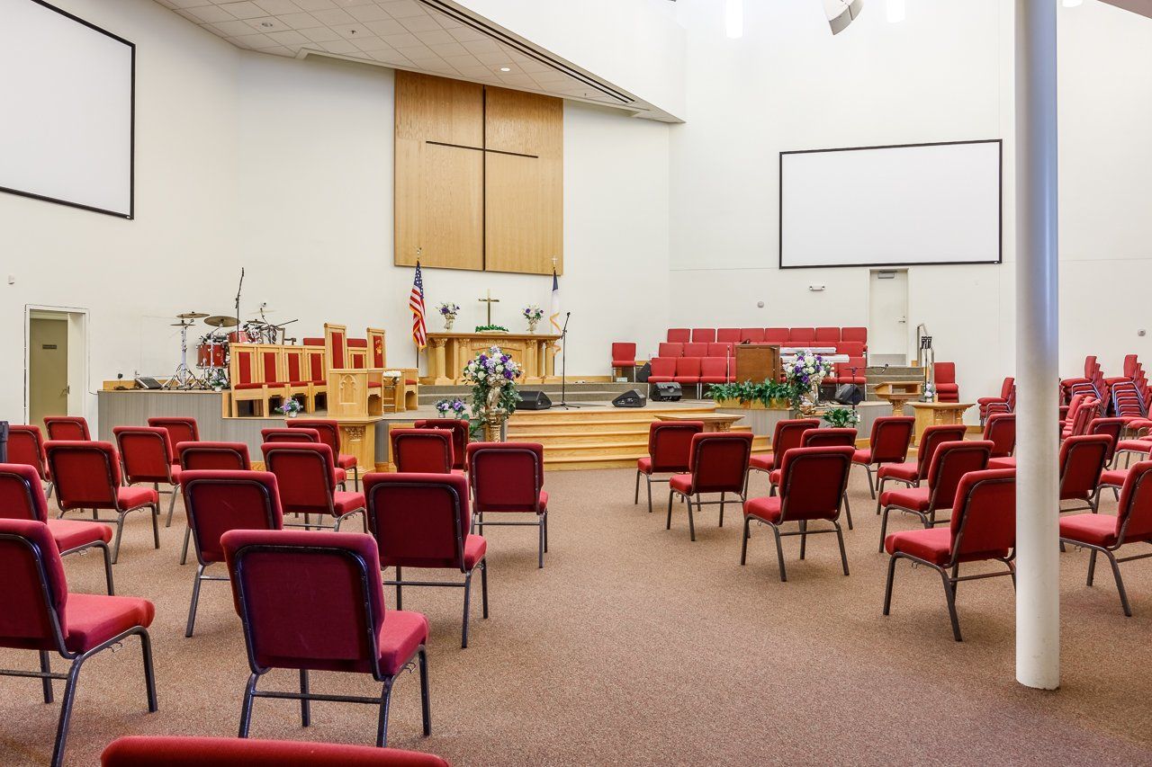 Empty church sanctuary with red chairs facing a stage with a podium and screens.