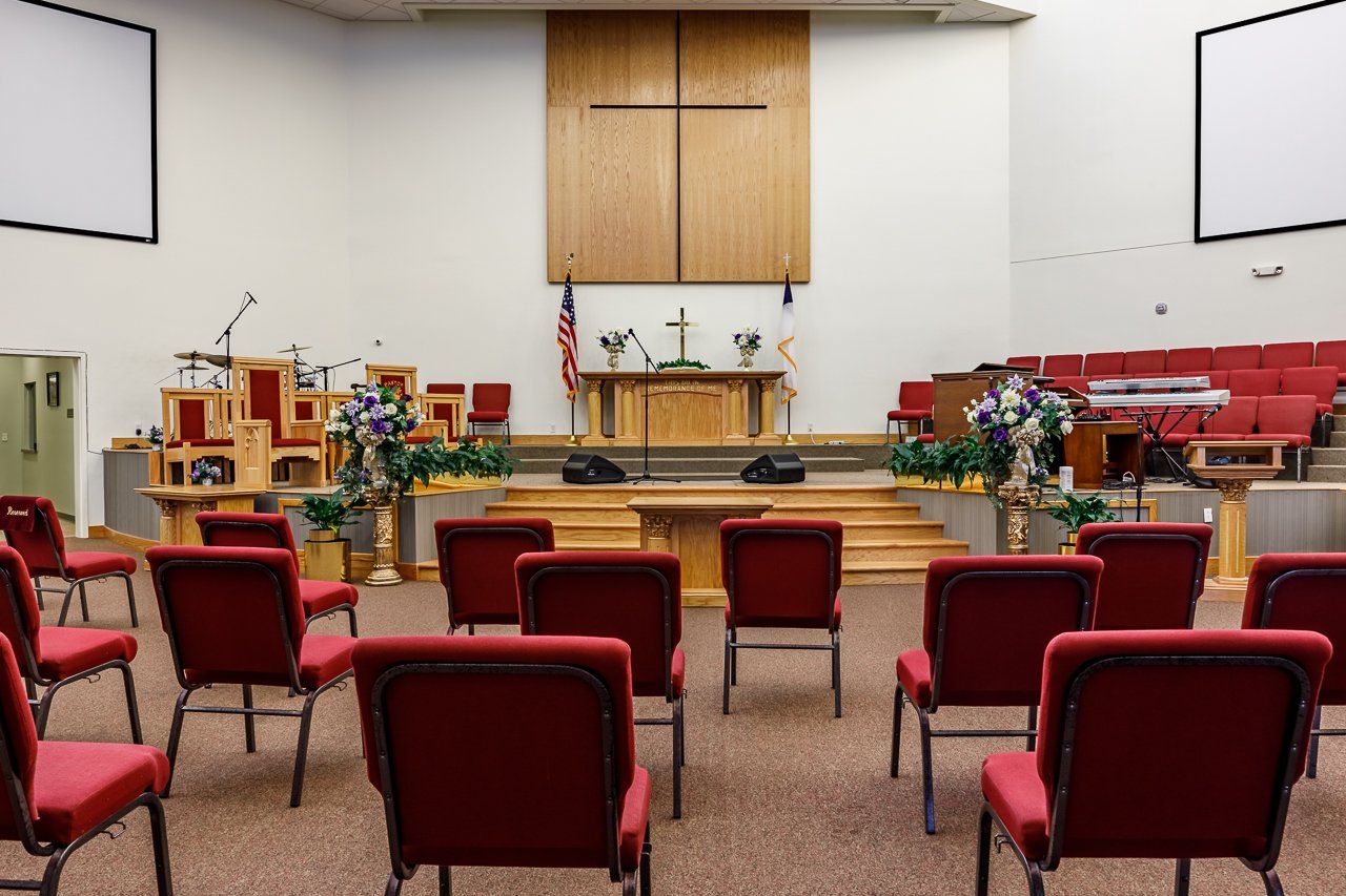 Interior view of a church sanctuary with red chairs, stage, wooden cross, and American flag.
