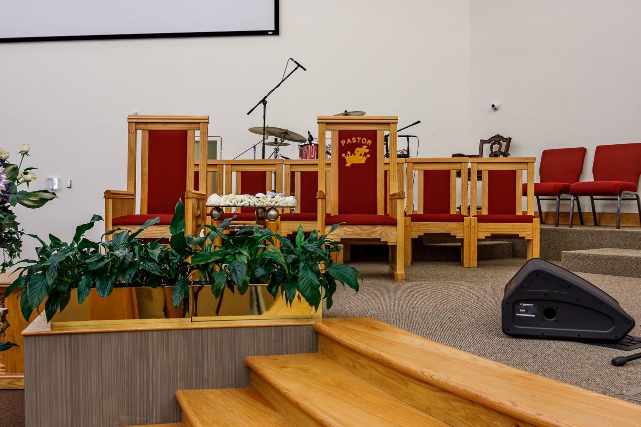 A church stage with wooden chairs, red upholstery, microphones, and a speaker, ready for a service.
