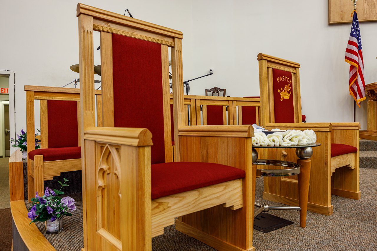 Wooden chairs with red cushions arranged in a church setting, small bouquet, and an American flag.
