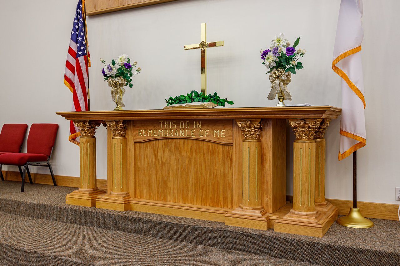 Wooden church altar with cross, flowers, American flag, and white flag with gold trim.