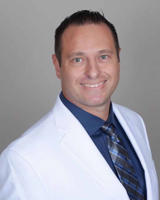 A woman is sitting at a desk with a laptop and a vase of flowers.