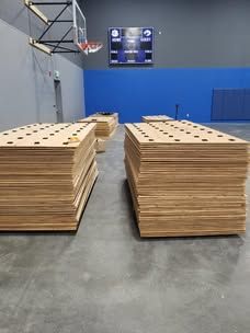 Two stacks of plywood are sitting in a gym next to a basketball hoop.