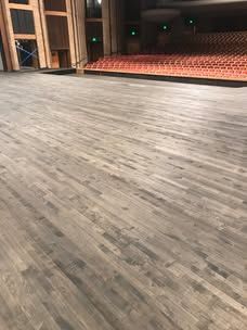 A wooden floor in an auditorium with a stage in the background.