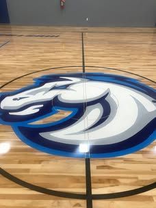A blue and white horse logo is painted on the floor of a basketball court.
