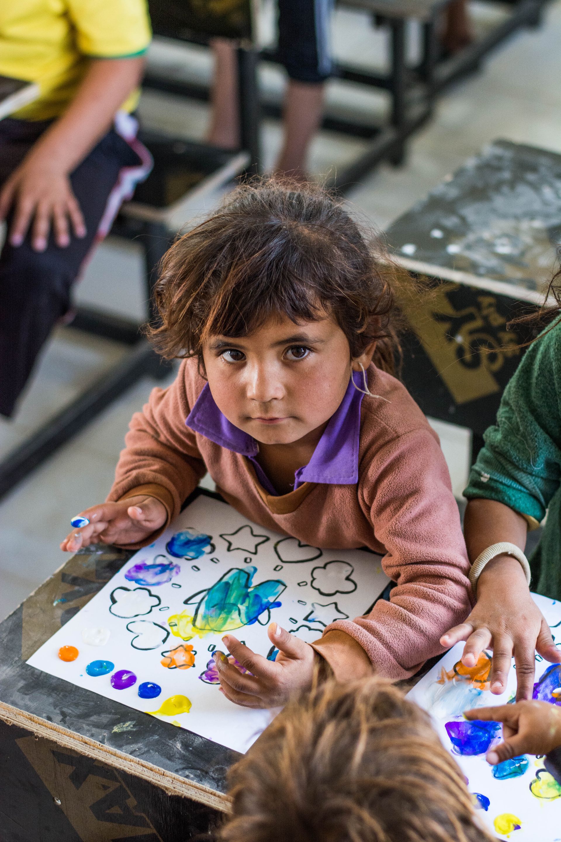 Humanitarian Programs in Iraq: A little girl is sitting at a table painting with her hands.