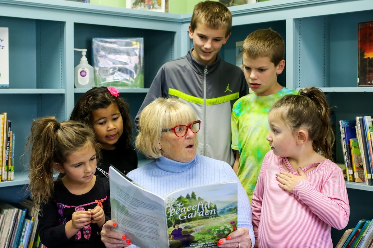 Programs for Refugees: A woman is reading a book to a group of children in a library.