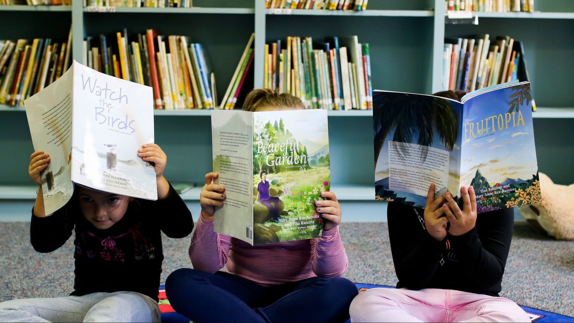 Alternatives to DEI Training: Three children are sitting on the floor reading books in a library