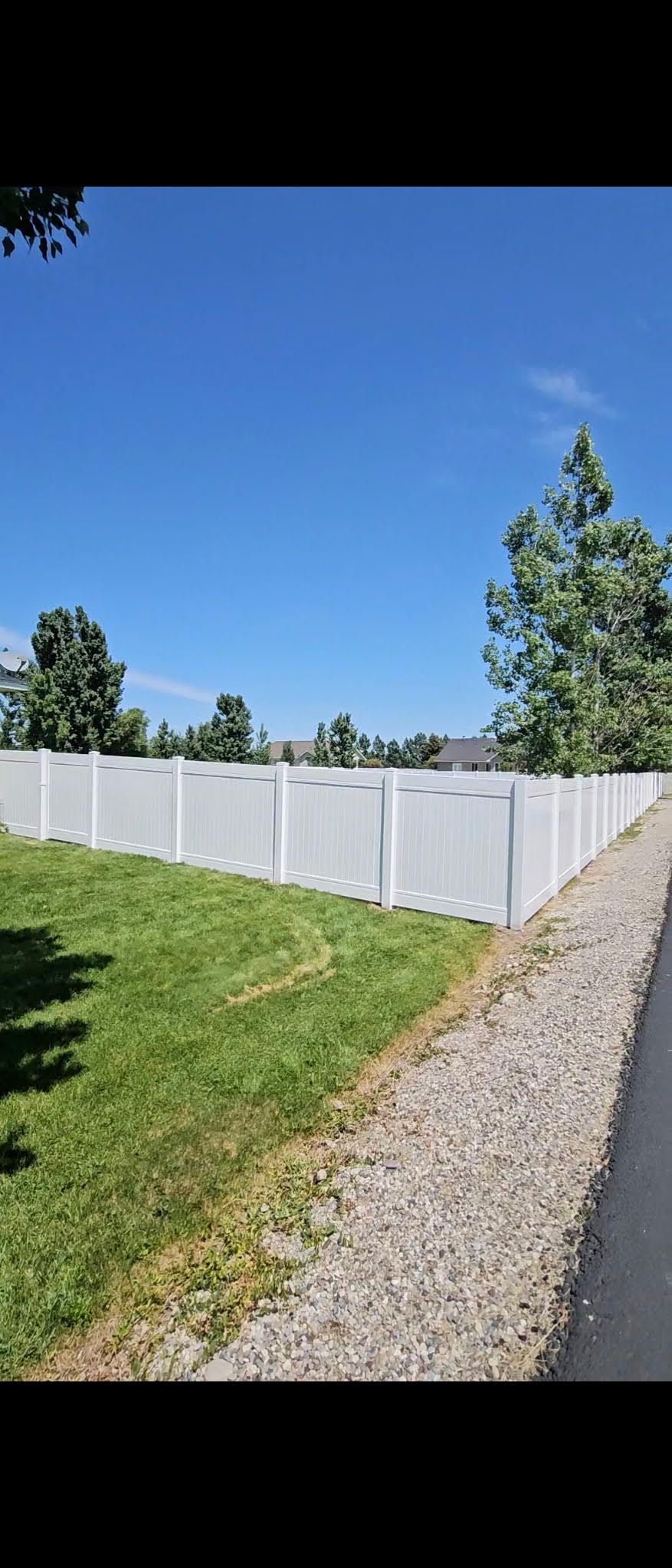 White vinyl fence beside a gravel path and green lawn under a clear blue sky
