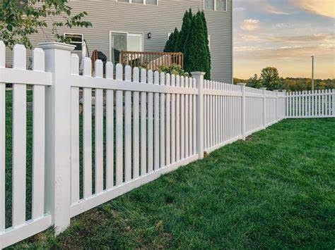 White vinyl picket fence along a green lawn beside a house at sunset
