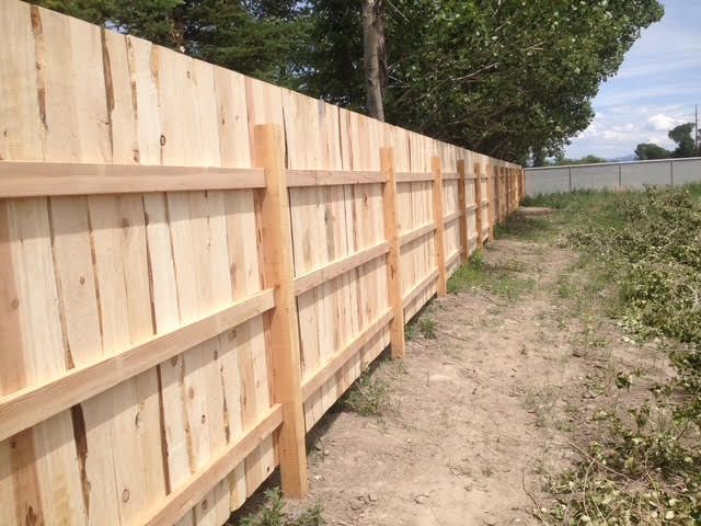Long wooden fence along a dirt path beside grassy yard and trees