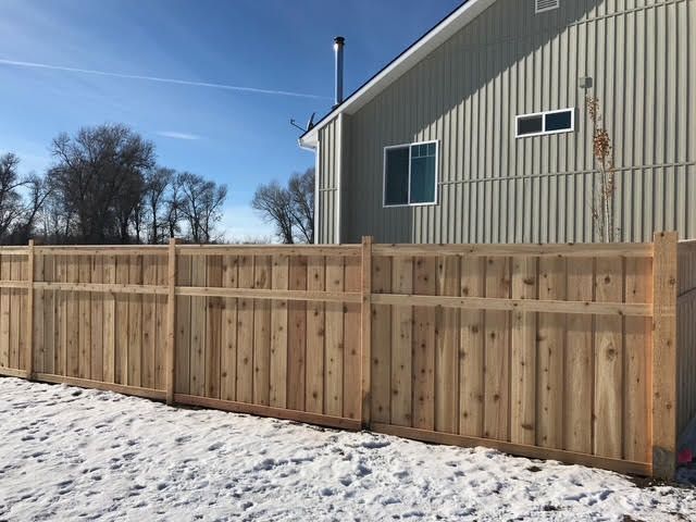 Wooden privacy fence in a snowy yard beside a beige house under a clear blue sky