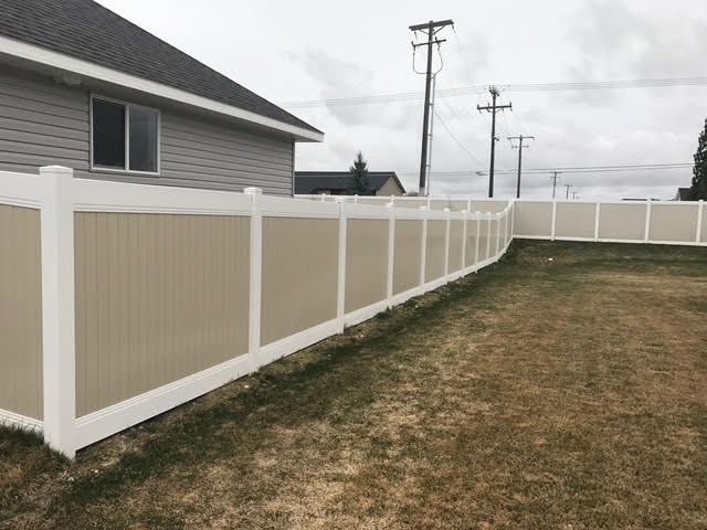 White vinyl fence along a beige house and grassy yard on an overcast day