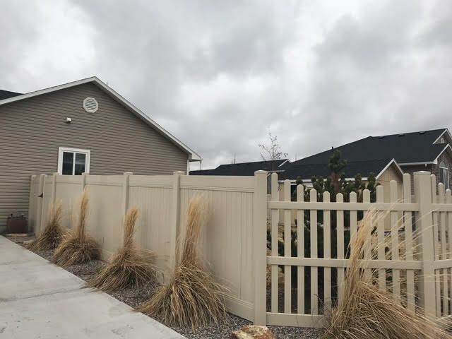Suburban house with beige fence and gate beside a driveway, under cloudy skies