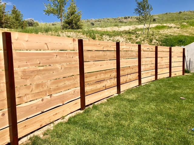 Wooden fence with dark posts along a grassy slope under a blue sky