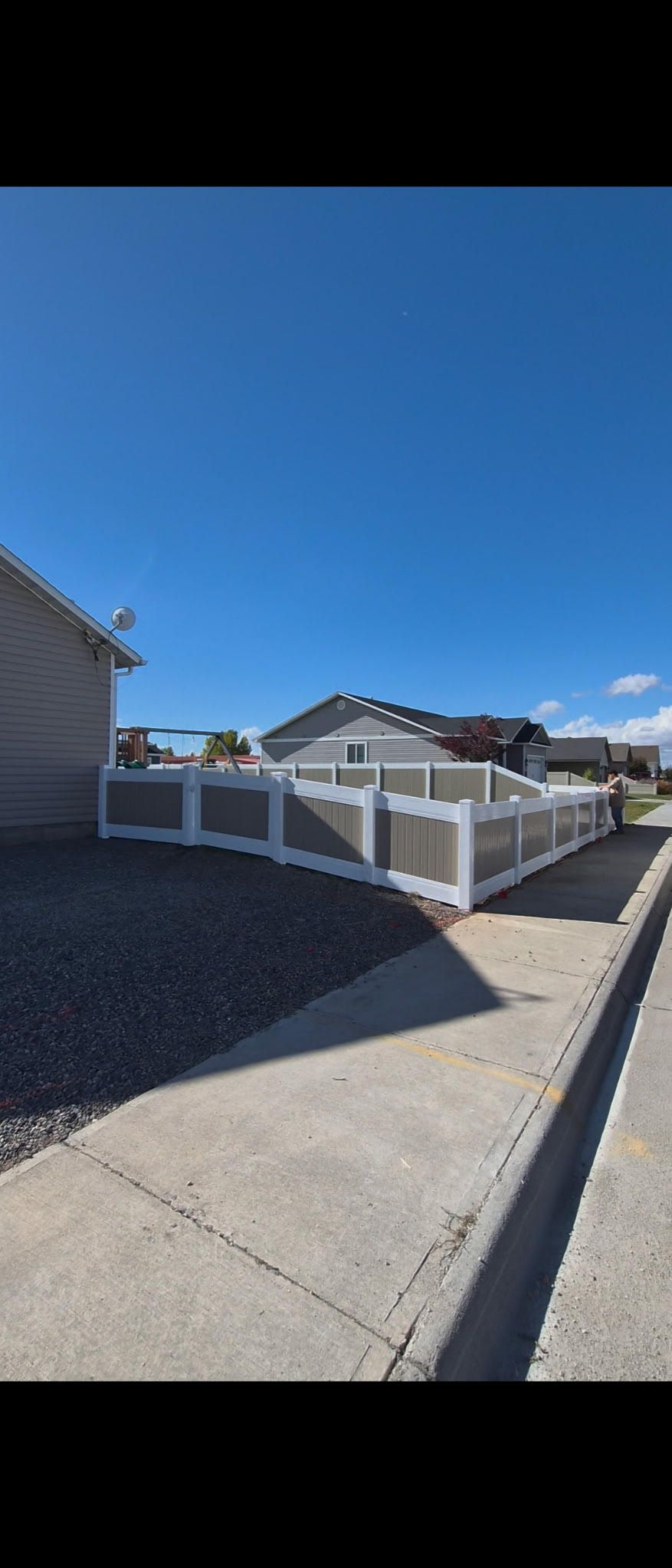 Sunny suburban street with houses, a white fence, and a blue sky